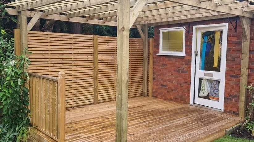 A pergola over decking with a slatted privacy screen
